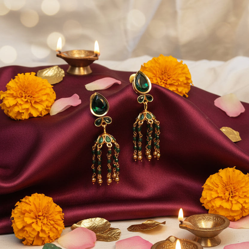 A pair of gold and green beaded dangle earrings displayed on a black jewelry stand against a wrinkled off-white fabric background.